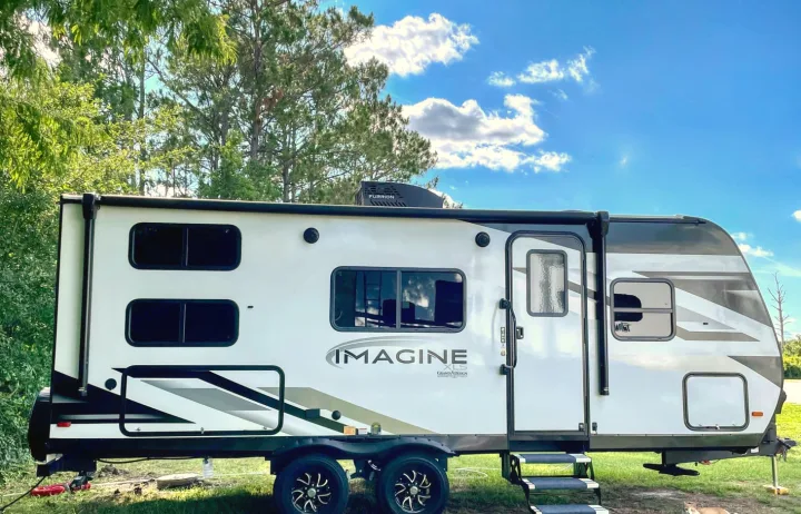 Modern Imagine XLS travel trailer, ideal for an rv rental, parked on grass. White and gray, under a blue sky with trees.. Grand Design Other 2023