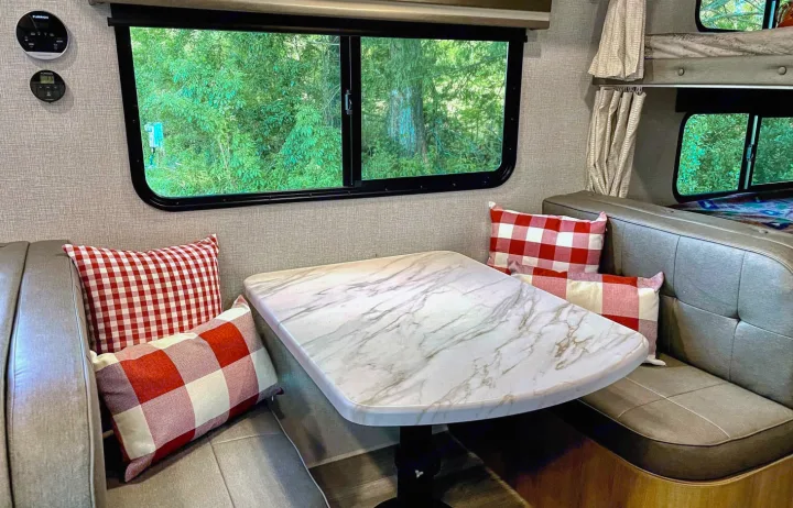 Cozy RV rental dinette with marble-look table, plaid pillows, and bunk beds. Perfect for family camping trips.. Grand Design Other 2023
