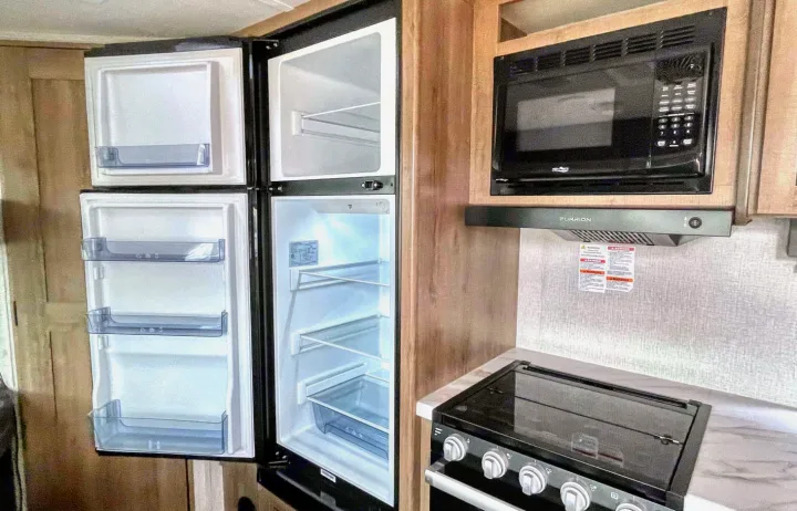 RV rental kitchen with open refrigerator/freezer, microwave, range hood, and stove. All set for adventure!. Grand Design Other 2023