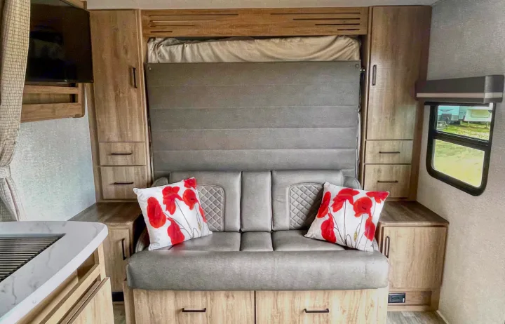 Light wood and gray interior RV rental with a pull-down murphy bed over the sofa, TV, and storage.. Grand Design Other 2023