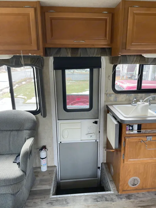 Experience this RV rental's cozy interior, featuring an armchair, kitchen sink, overhead cabinets, and entrance with a floor hatch.. Fleetwood Fiesta 2005