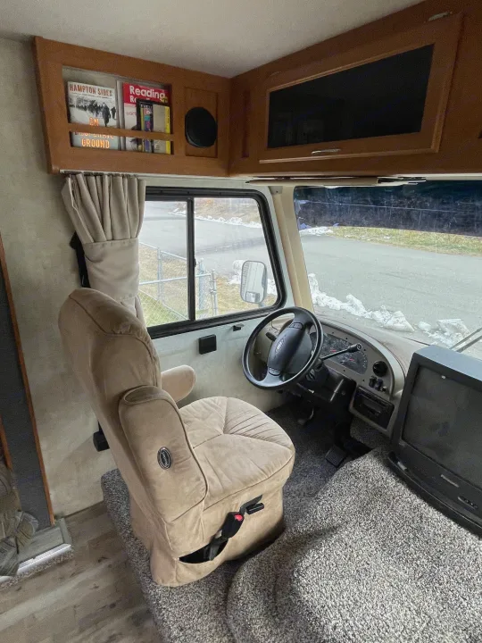 RV rental cockpit: plush driver's seat, dashboard, and windshield view of a snowy road. Overhead storage visible.. Fleetwood Fiesta 2005