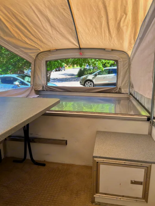 Inside an RV rental: Cozy pop-up camper interior with table, bed, and outdoor views for camping and travel.. Quicksilver Quicksilver Livin Lite 2011