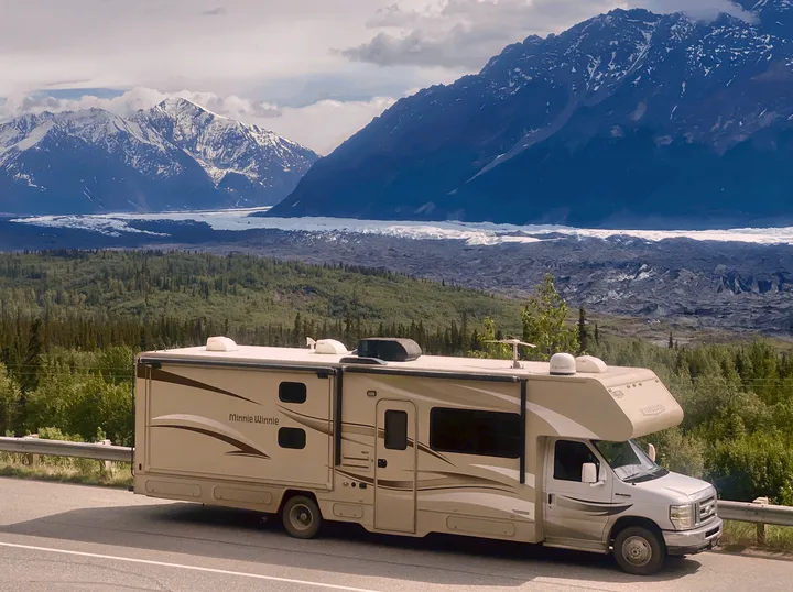 An RV rental (Minnie Winnie) is parked roadside, with a vast glacier and snow-capped mountains in the background.. Winnebago Minnie Winnie 2015