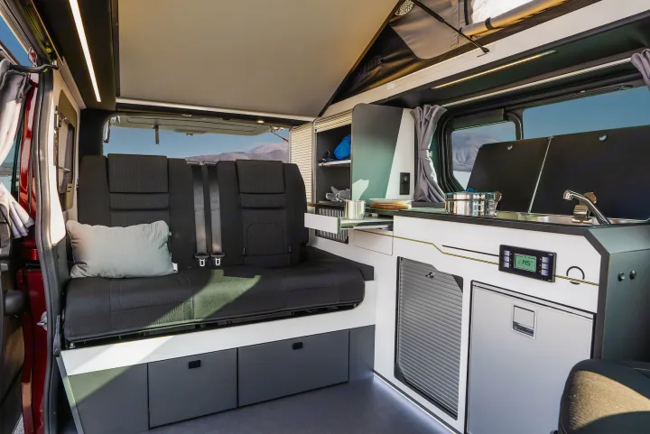 Inside an RV rental: a modern camper van interior featuring a multi-purpose bench, integrated kitchenette, and fridge.. HANROAD TREK 4 2023