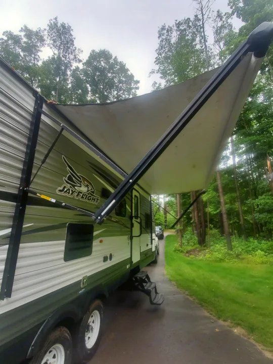 Jay Flight RV rental parked with its awning extended in a wooded setting, ready for camping adventures.. Jayco Jay Flight 2018
