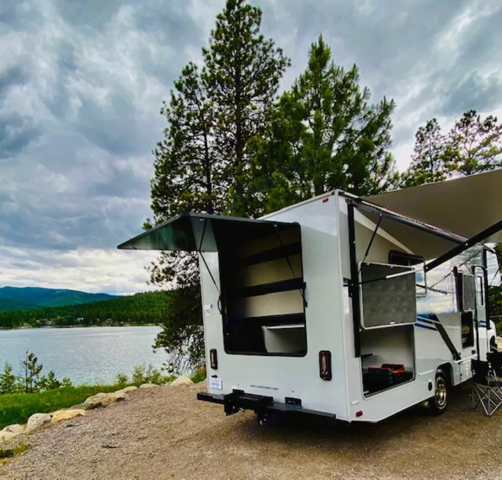 An RV rental parked lakeside with rear hatch & side bays open, showing ample storage for gear & toys.. Forest River Coachmen Cross Trail XL 2022