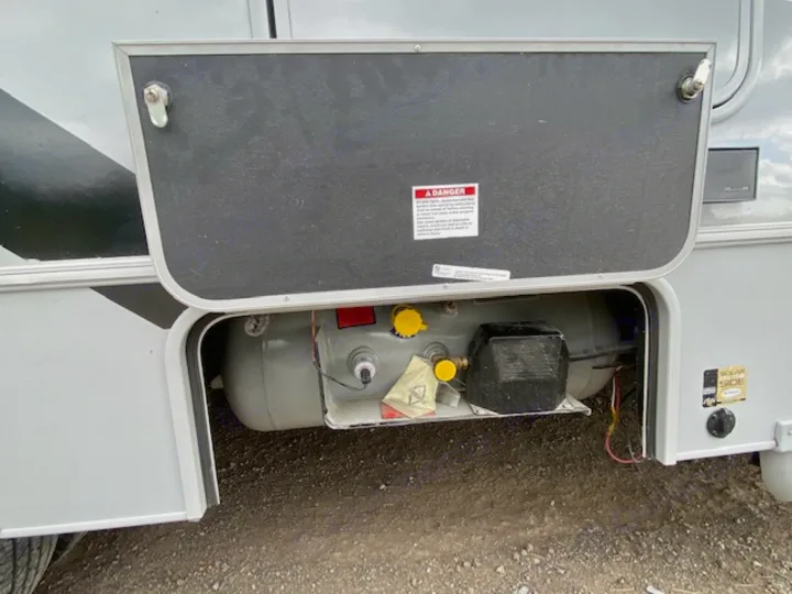 An RV rental's open exterior storage compartment reveals a large, gray propane tank. A "DANGER" label is on the door.. Forest River Coachmen Cross Trail XL 2022