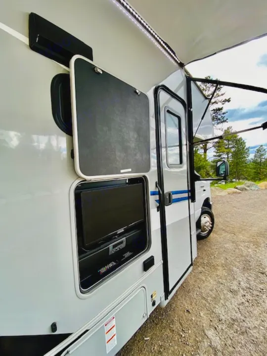 This rv rental features an exterior entertainment center with a TV and an illuminated awning on its side.. Forest River Coachmen Cross Trail XL 2022