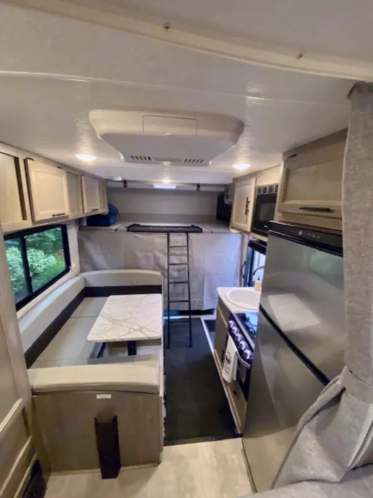 Spacious RV rental interior featuring a cozy dining booth, full kitchen, and an accessible overhead sleeping area.. Forest River Coachmen Cross Trail XL 2022
