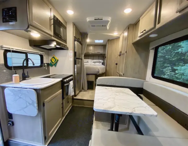 Bright RV rental interior showing a kitchen, dining area with a table, and a bed further back.. Forest River Coachmen Cross Trail XL 2022