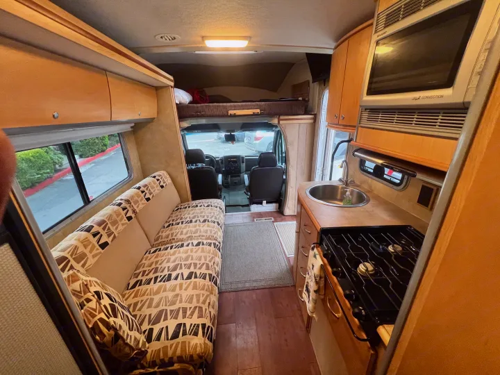 Spacious RV rental interior with kitchen (sink, stove, microwave), sofa, and overhead bunk area for comfortable travel.. Winnebago View 2008