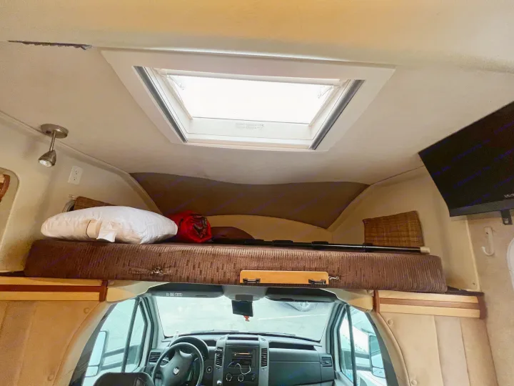 RV rental interior: cozy cabover bunk with skylight, and the front driving area with steering wheel.. Winnebago View 2008