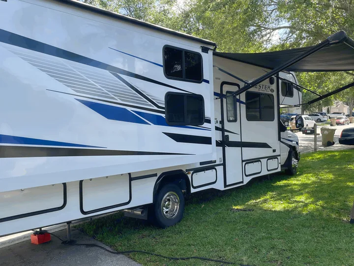 White **RV rental** with blue/black graphics & extended awning, parked on grass for camping.. Forester LE 2023