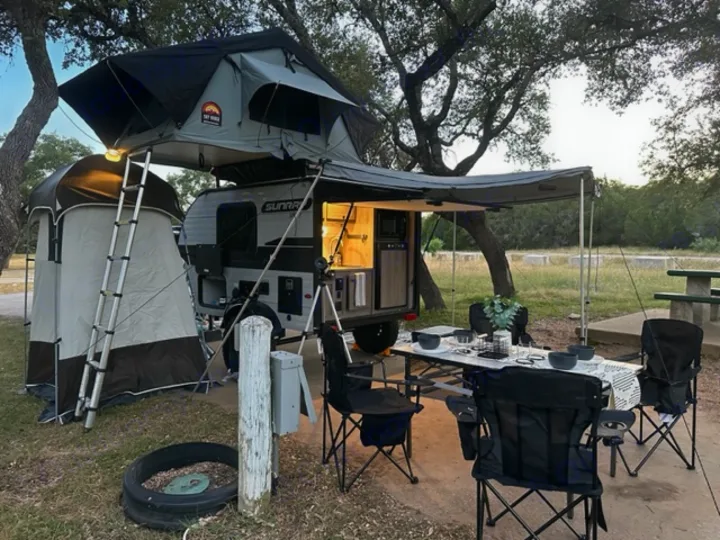 Modern RV rental camping setup: rooftop tent, outdoor kitchen, and dining area under an awning in nature.. Sunset Park RV SunRay 2023