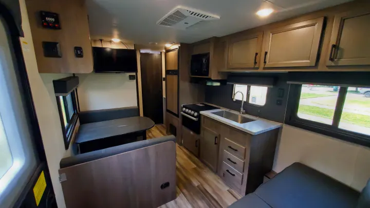 Inside this modern RV rental: a well-lit kitchen with sink, stove, and microwave, plus a dinette and TV.. Starcraft Autumn Ridge 2022