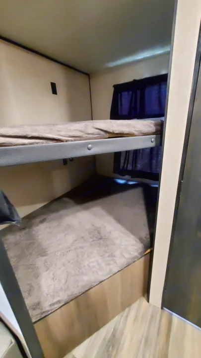 Inside an RV rental: cozy bunk beds with mattresses, privacy curtains, and laminate flooring for compact sleeping.. Starcraft Autumn Ridge 2022