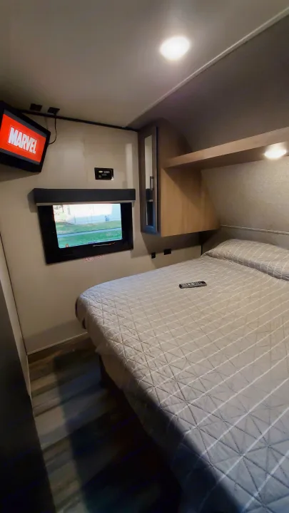 Cozy RV rental bedroom with a quilted bed, TV, window (with exit sign), and storage. Ready for adventure!. Starcraft Autumn Ridge 2022