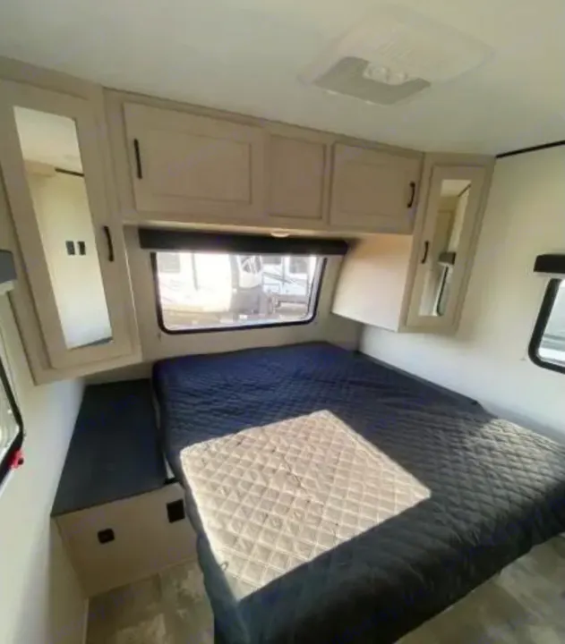 Spacious RV rental bedroom featuring a bed, overhead cabinets, windows, and an AC unit.. Coachmen Other 2022