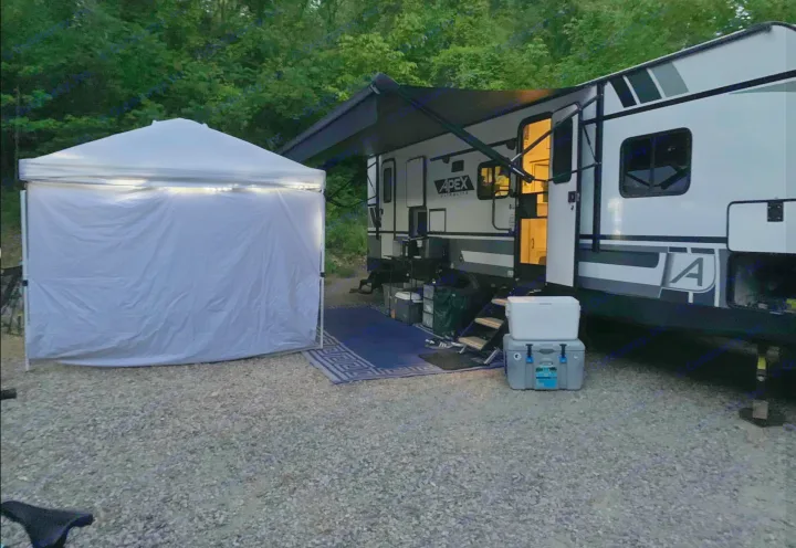 An RV rental is parked at an illuminated gravel campsite with an extended awning and a lit white pop-up canopy nearby.. Coachmen Other 2022