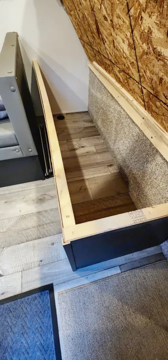 RV rental: Built-in bed base with grey textured sides & wood-look floor. An OSB wall and a grey sofa complete this camper setup.. Keystone RV Springdale 2022