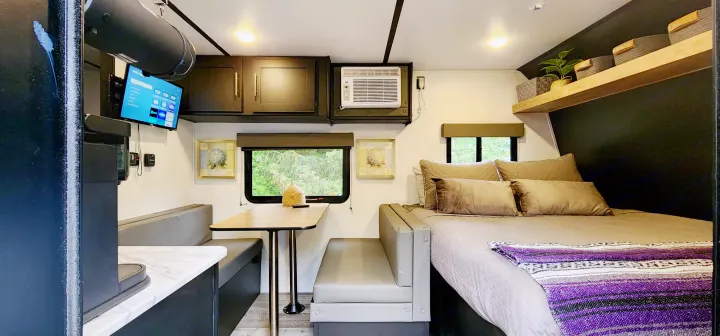 Explore this cozy rv rental interior featuring a comfortable bed, dining booth, wall-mounted TV, and modern amenities.. Keystone RV Springdale 2022