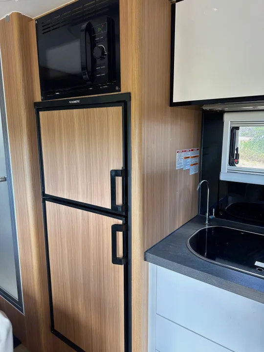 Inside an RV rental: a compact kitchen with a Dometic fridge, microwave, sink, and window view.. Black Series Black Series Trailer 2022