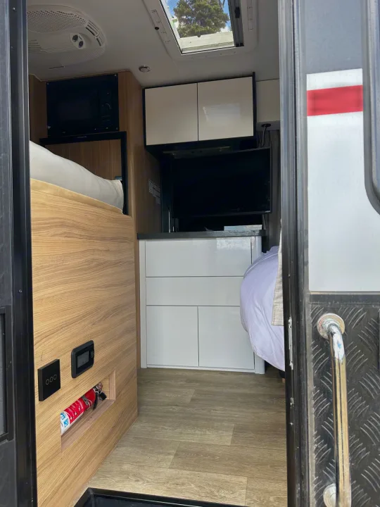 Modern RV rental interior: features two sleeping areas, compact kitchen with microwave, light wood, white cabinetry, and smart storage.. Black Series Black Series Trailer 2022