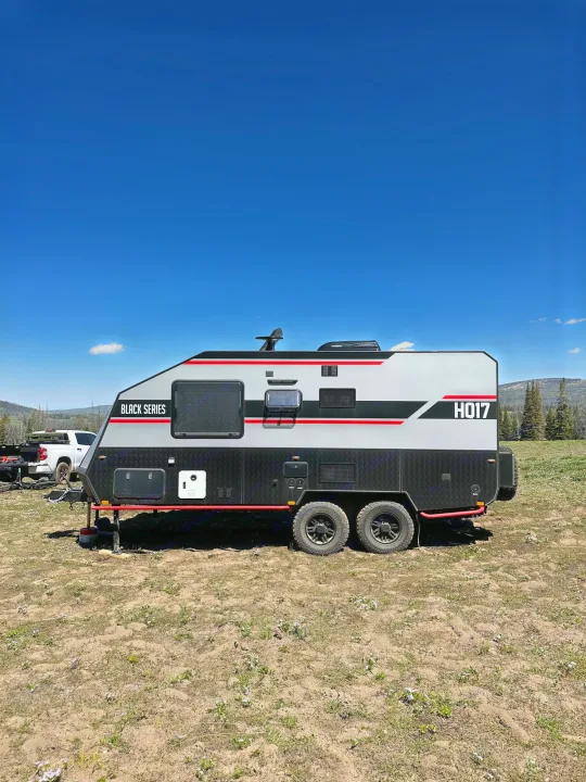 Black Series HQ17 off-road travel trailer, perfect for RV rental adventures, parked in a sunny, scenic outdoor camp.. Black Series Black Series Trailer 2022