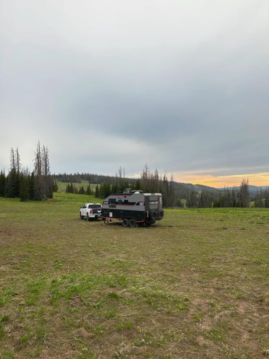 Off-road RV rental and truck parked in a large field. Ideal for remote camping and outdoor exploration at sunset.. Black Series Black Series Trailer 2022