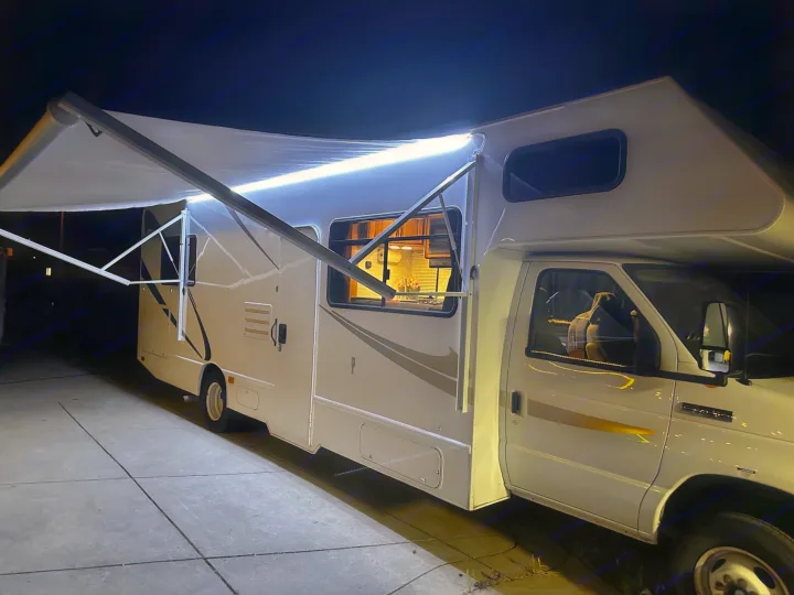 An inviting RV rental at night, brightly lit under its extended awning, ready for adventure or a cozy stop.. Thor Majestic 2015