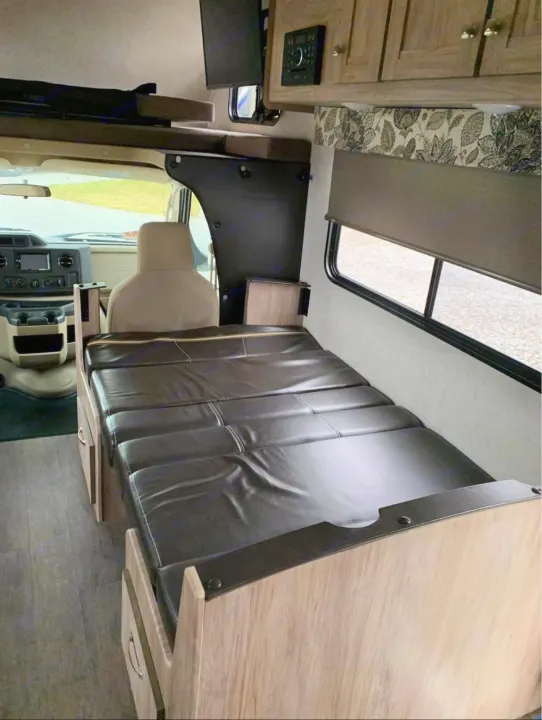 RV rental interior view: large convertible bed with dark cushions, light wood cabinets, and front driving area.. Forester LE 2018