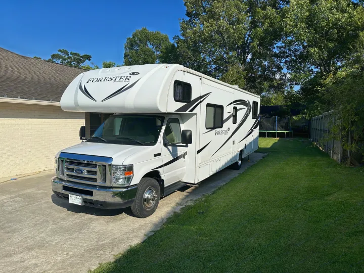 White Class C Forester **RV rental** parked on a paved driveway beside a house, with a grassy yard & trees. Ready for travel!. Forester LE 2018