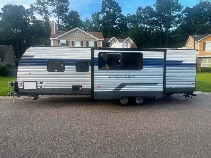 Large silver/blue Avenger travel trailer with extended slide-out, parked on asphalt. Perfect for RV rental.. Forest River Prime time Avenger 2023
