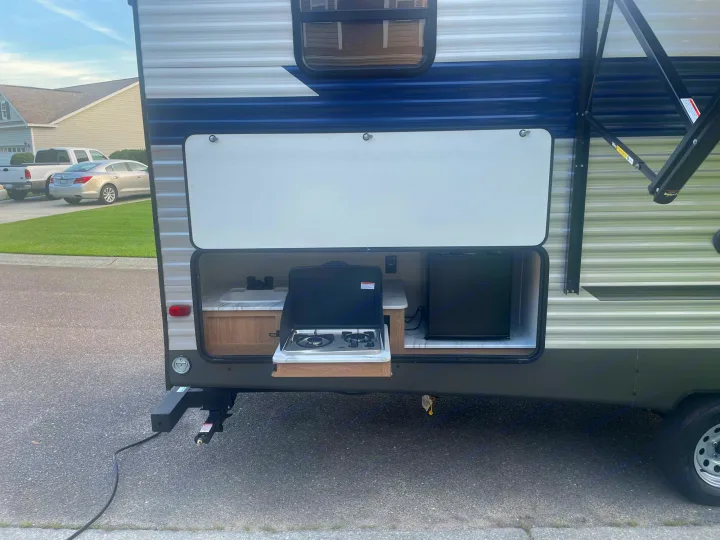 This RV rental's outdoor kitchen features a sink, stove, and mini-fridge, perfect for your next camping adventure.. Forest River Prime time Avenger 2023
