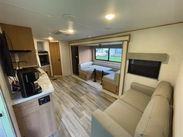 Inside a cozy RV rental: living area with sofa, dinette, kitchen counter, and glimpse of bunk beds.. Forest River Prime time Avenger 2023