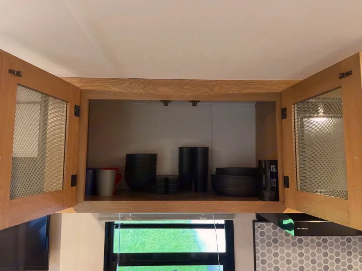 Organized **RV rental** kitchen cabinet with black dishes, cups, and a window view to green grass.. Forest River Prime time Avenger 2023