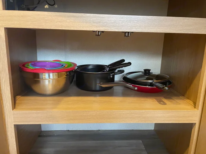Organized kitchenware in an RV rental cabinet: nesting bowls with colorful lids, pots, and pans neatly stored.. Forest River Prime time Avenger 2023