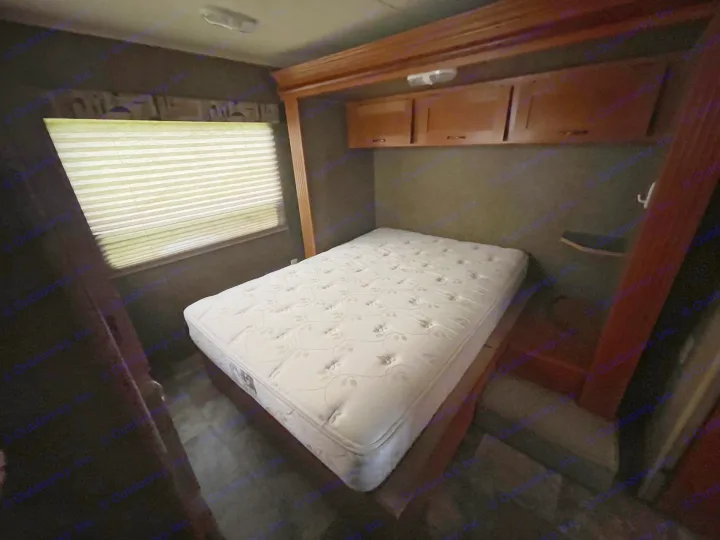 Compact RV rental bedroom with a white mattress, overhead wooden cabinets, and window with closed blinds. Functional interior.. Forest River Cherokee Grey Wolf 2015