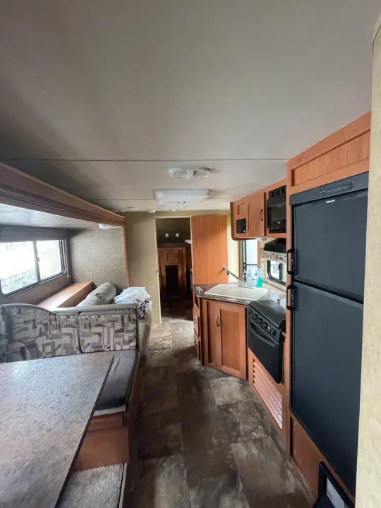 RV rental interior featuring a kitchen with fridge/stove, dining area with seating, and a view into the back sleeping quarters.. Forest River Cherokee Grey Wolf 2015