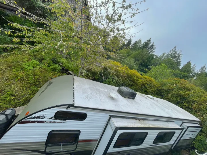 RV rental parked in lush nature. Image shows the camper's roof with AC unit and stained side with windows.. Forest River Cherokee Grey Wolf 2015