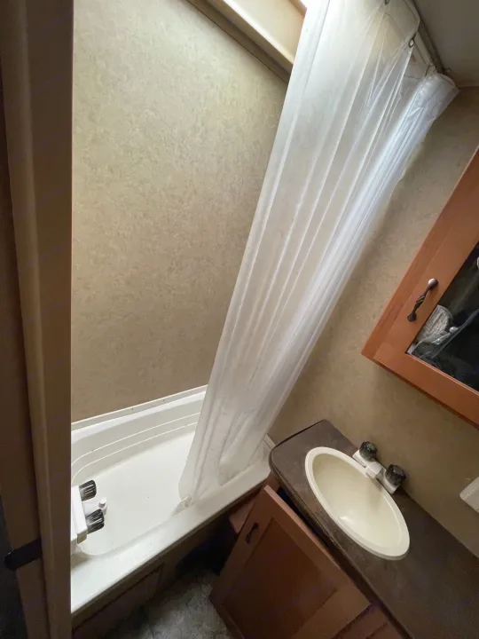 RV rental bathroom interior: Features a small shower/tub, sink with vanity, & mirrored cabinet.. Forest River Cherokee Grey Wolf 2015