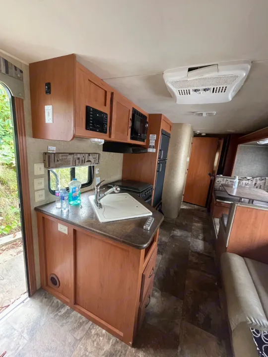 Inside this RV rental: kitchen with sink, microwave, stove, fridge, dining booth, and sofa. Modern travel amenities.. Forest River Cherokee Grey Wolf 2015