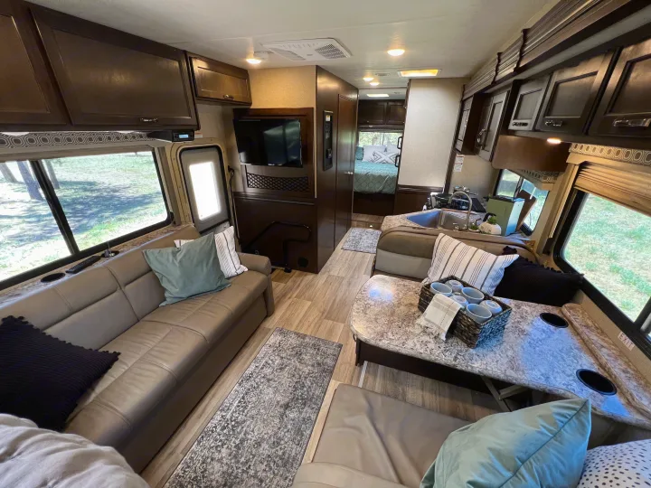 Spacious, modern RV rental interior features a cozy living area, dining booth, and kitchen. View into the bedroom.. Thor Four Winds 2020