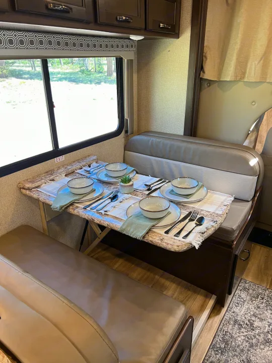 An RV rental's inviting dinette with a set table, four place settings, and scenic window views. Perfect for onboard dining.. Thor Four Winds 2020