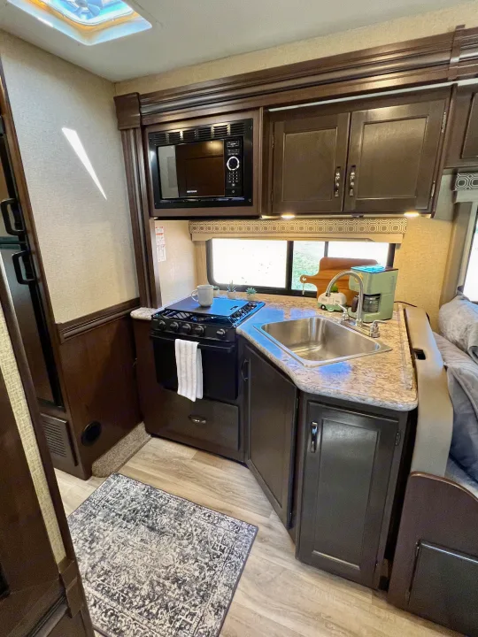 RV rental kitchen with stove, sink, microwave, and cabinets, ready for cooking on the road.. Thor Four Winds 2020