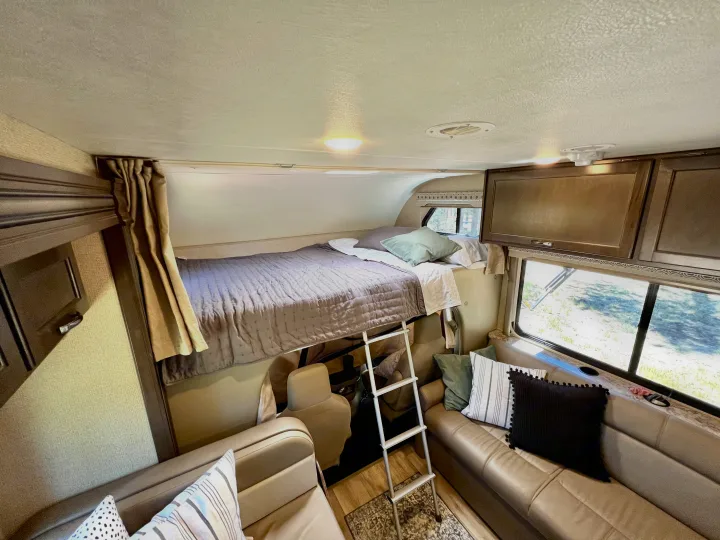 Cozy RV rental interior with a spacious bunk bed above the comfortable living area, perfect for adventurers.. Thor Four Winds 2020