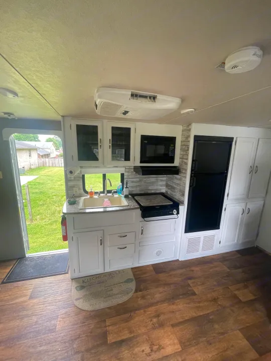Inside a clean RV rental: full kitchen with white cabinets, modern appliances, and wood flooring. Ready for adventures!. Forest River Wildwood X-Lite 2016