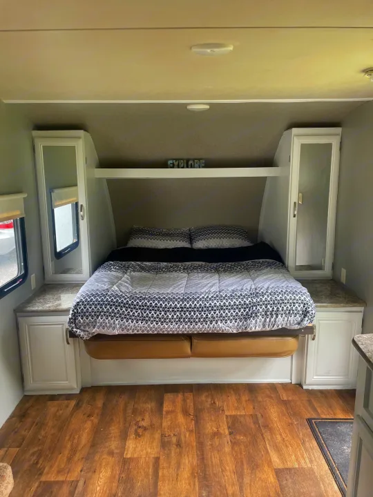 Cozy RV rental bedroom: a bed with geometric bedding, mirrored side cabinets, and wood-look flooring. Ready for travel!. Forest River Wildwood X-Lite 2016