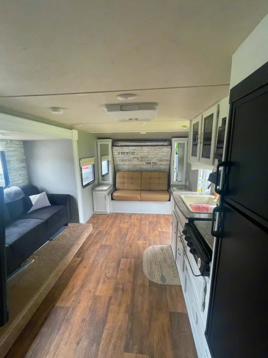 Explore this bright rv rental interior, featuring a cozy sofa, kitchen, bunk bed, and wood-look floors. Perfect for travel!. Forest River Wildwood X-Lite 2016